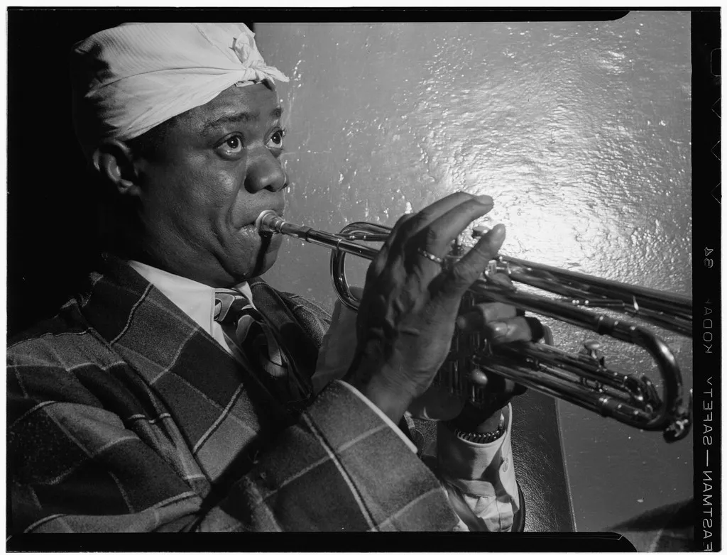 Louis Armstrong playing trumpet in a white head kerchief at the Aquarium jazz club, New York, 1946.