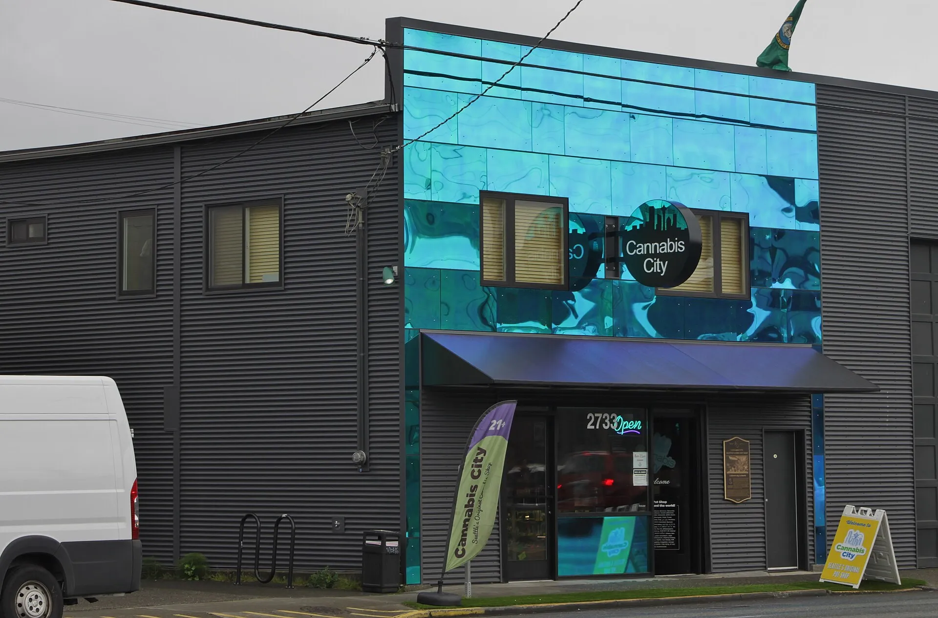 The teal-mirrored storefront of Cannabis City in Seattle with a 21+ banner by the door.