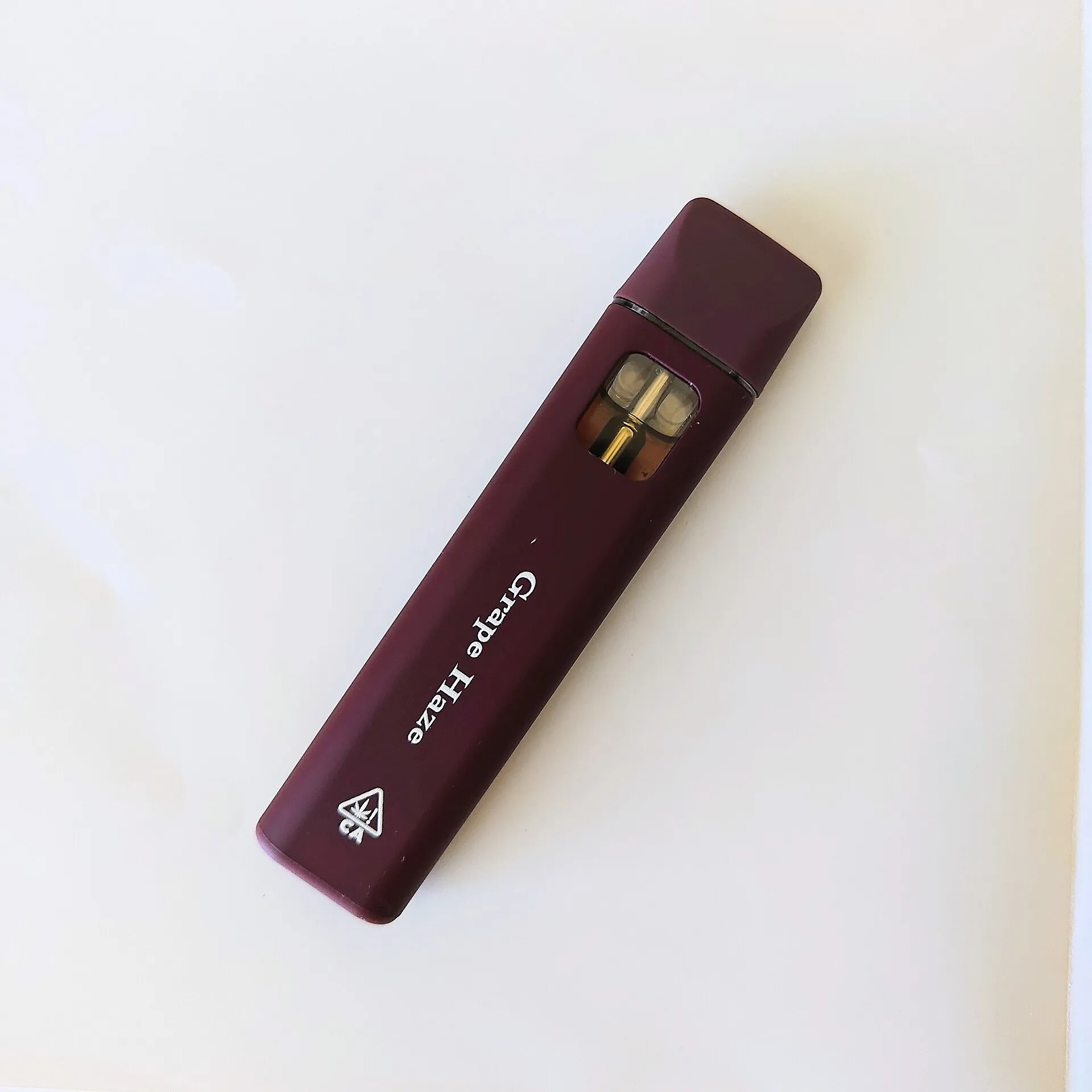 A single dark-red disposable cannabis vaporizer lying flat on a plain off-white surface.