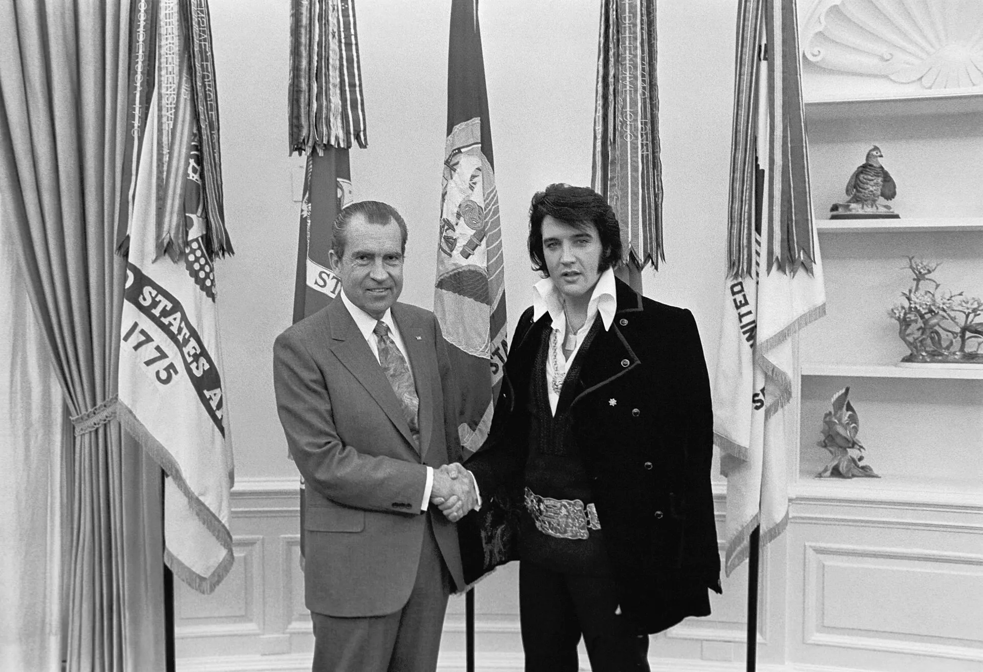Richard Nixon shakes hands with Elvis Presley among flags in the Oval Office in December 1970.