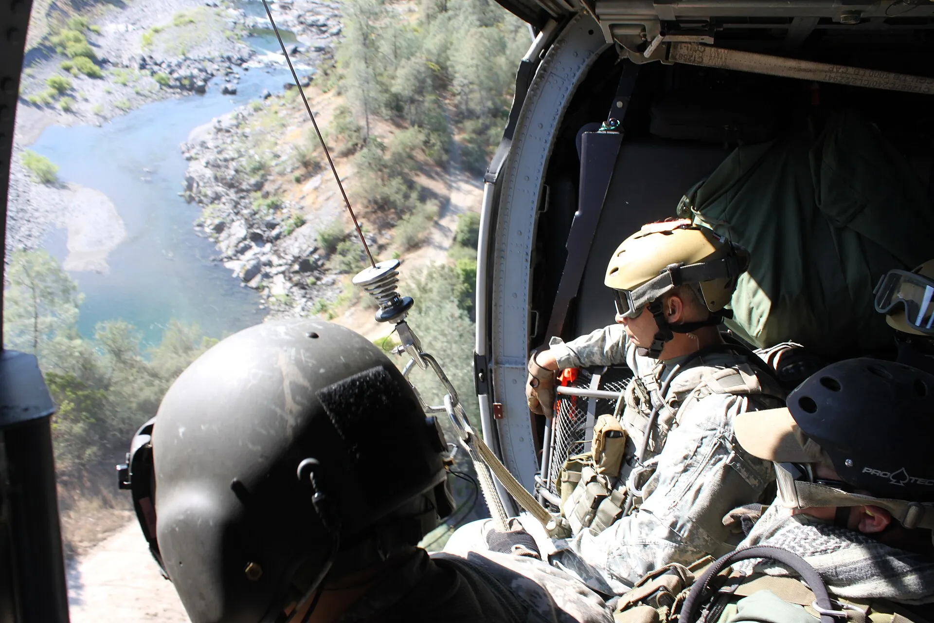 National Guard members look down from the open door of a hovering helicopter above a river canyon during a marijuana-eradication operation.