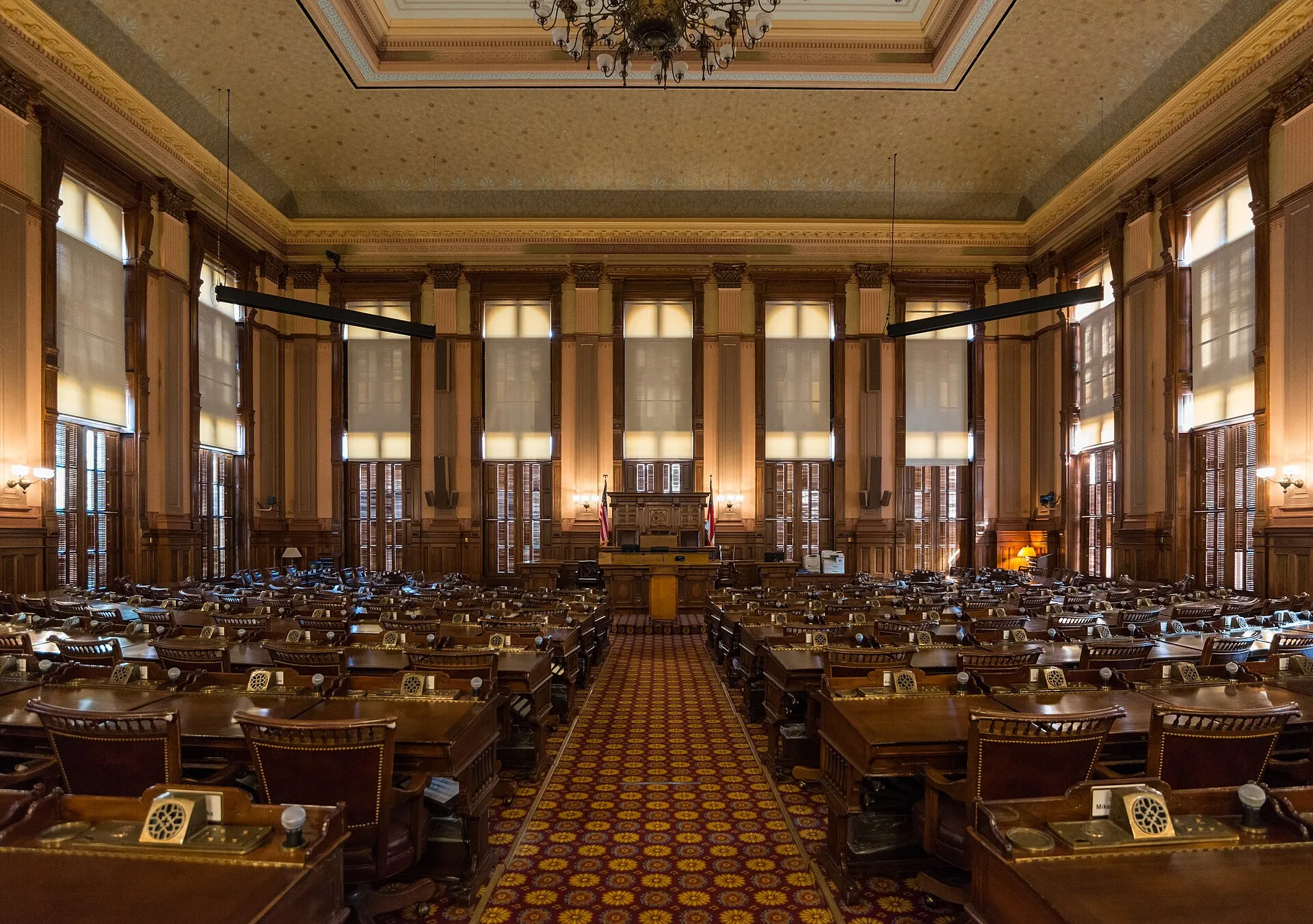 The House of Representatives chamber in the Georgia State Capitol, with rows of wooden desks and a patterned red carpet.