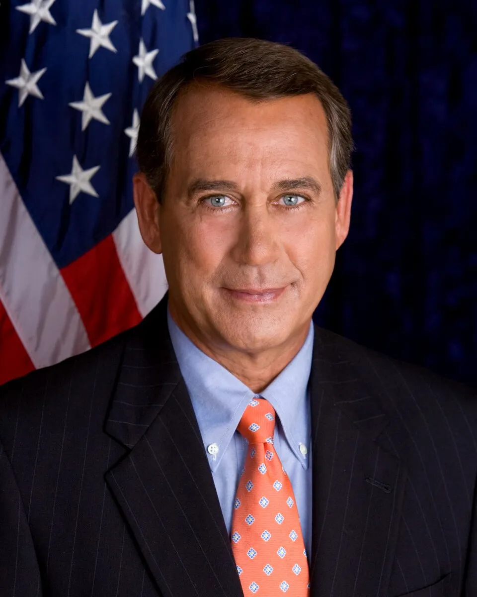 Official portrait of John Boehner in a dark suit and orange tie in front of the American flag.