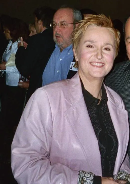 Melissa Etheridge smiling at an event in a pale jacket.