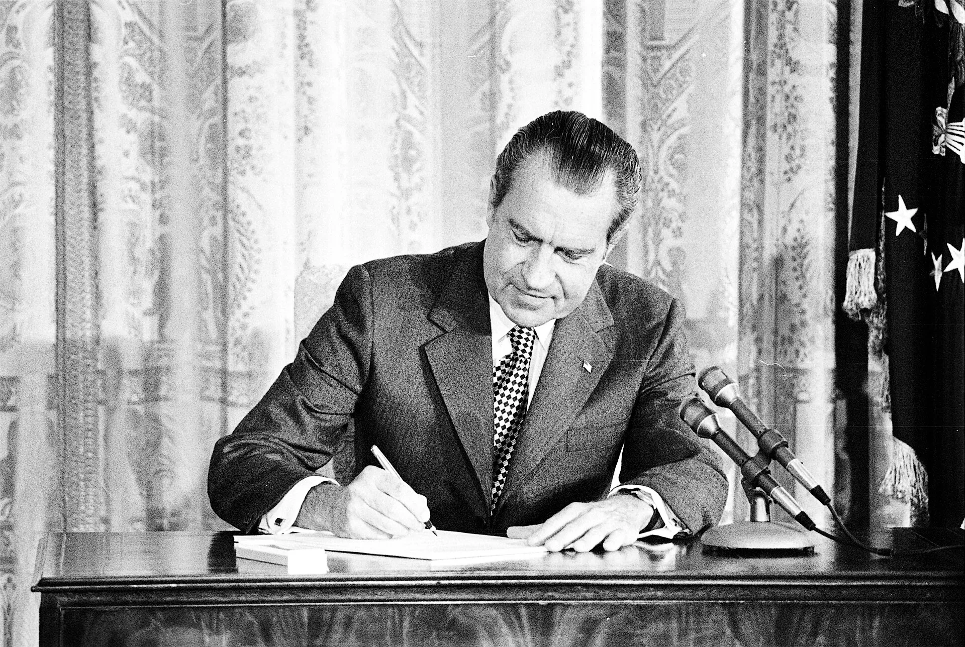 President Nixon, seated at a desk before microphones, signs the Drug Abuse Office and Treatment Act in March 1972.