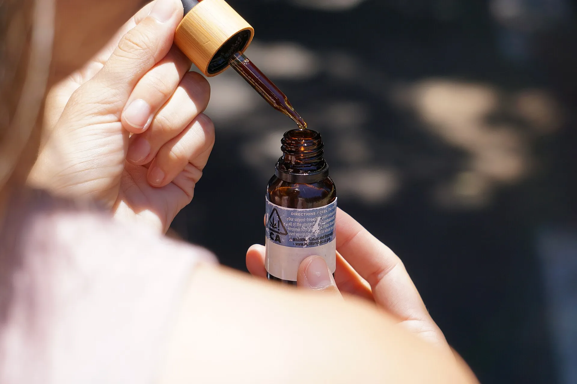 Close-up of hands drawing a measured dropper of amber cannabis oil from a small labeled tincture bottle.