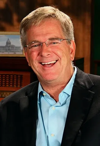 Rick Steves smiling in glasses and a dark blazer.