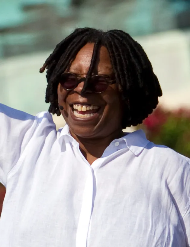 Whoopi Goldberg laughing outdoors in a white shirt.